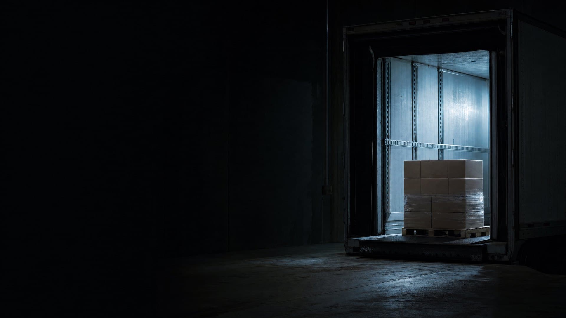 A loaded pallet at the open door of a refrigerated trailer on a dark loading dock