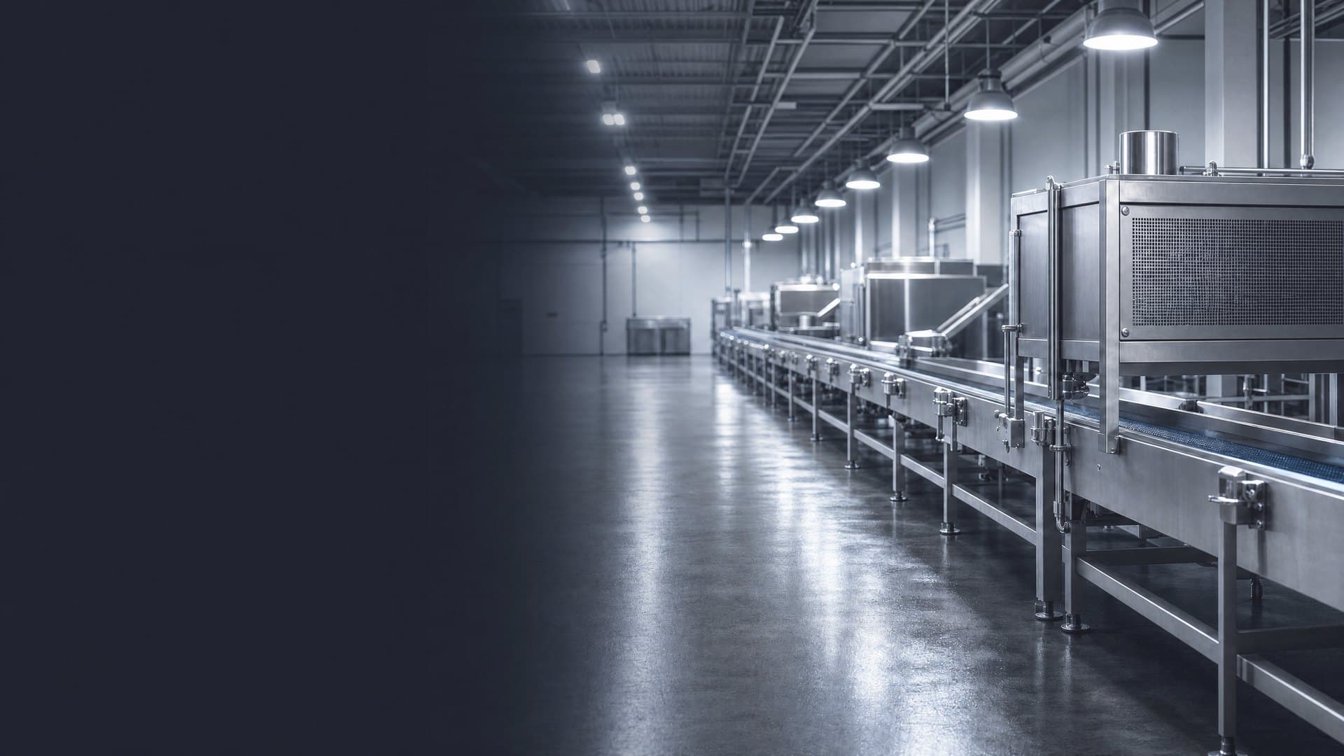 A stainless-steel conveyor line in a food processing plant at the start of a shift, its overhead lights switched on down the line